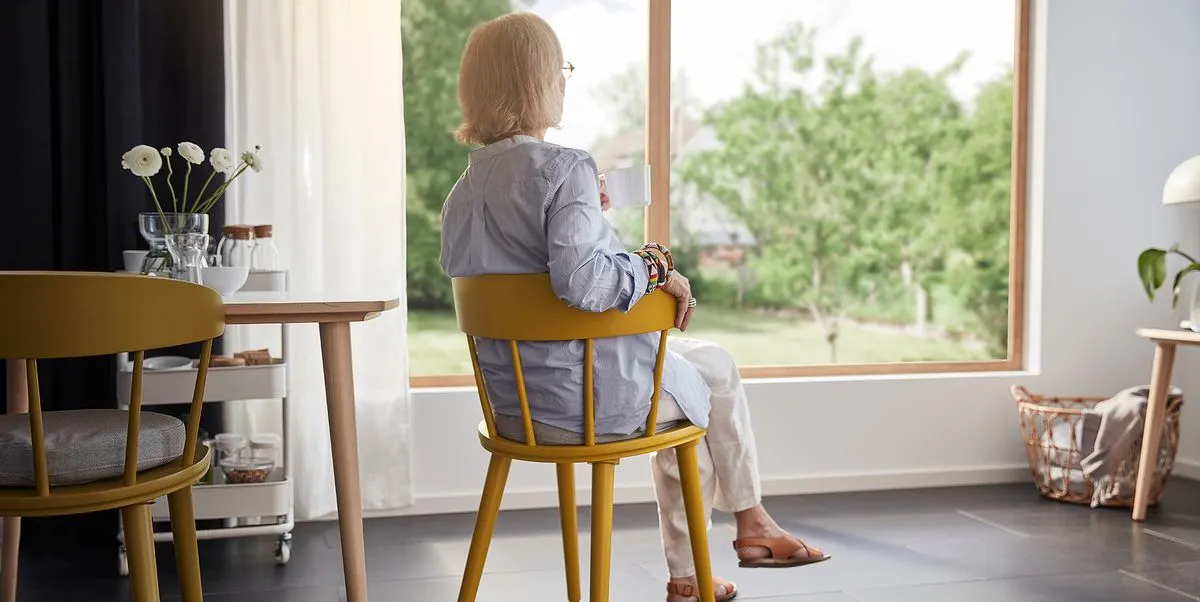 Mujer mayor tomando café junto a una ventana de su salón