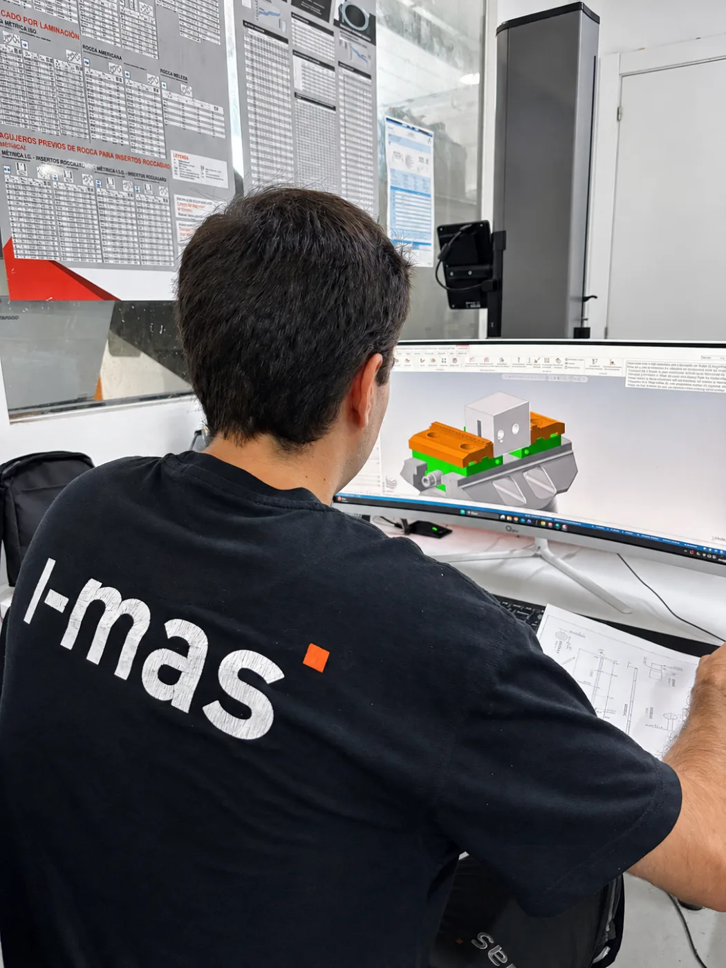 Técnico de i-mas programando en CAM el amarre y el mecanizado de una pieza, con el plano sobre la mesa