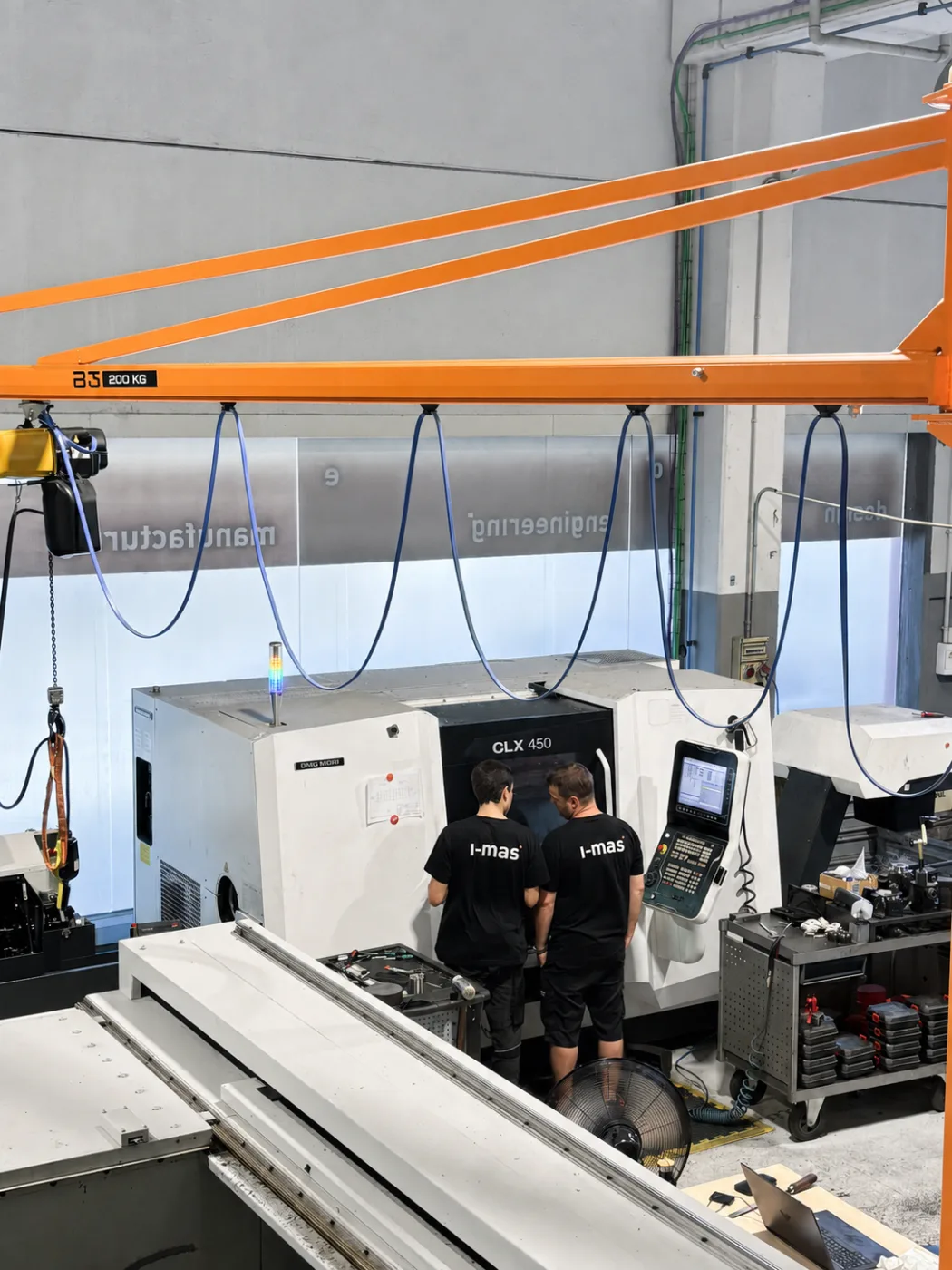 Dos técnicos de i-mas en el torno DMG MORI CLX 450, bajo el puente grúa del taller
