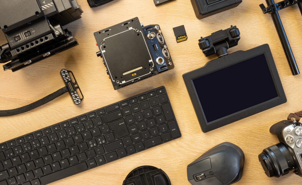 Flat lay of filming equipment with keyboard and mouse. Overhead view of video camera with computer parts on table. Directly above shot of various accessories arranged on surface.